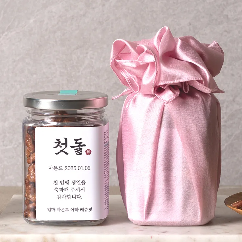 '첫돌' 라벨이 붙은 보틀과 핑크 보자기로 감싼 답례품