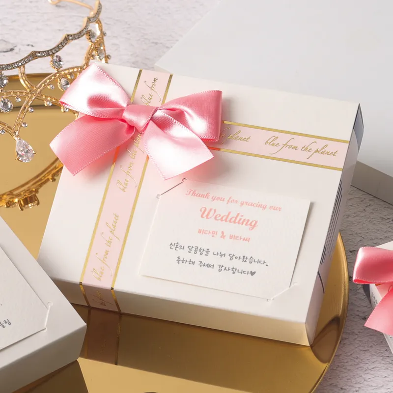 티아라 옆에 놓인 핑크 리본 비타민 답례품 상자와 웨딩 감사 카드